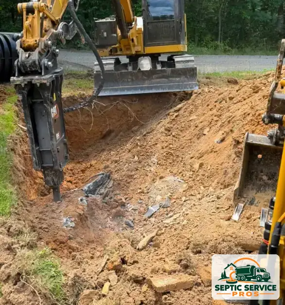 Excavator with a hydraulic breaker digging through rock for a septic tank install