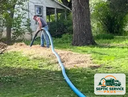 Technician running a long pump hose across a yard to reach a septic tank